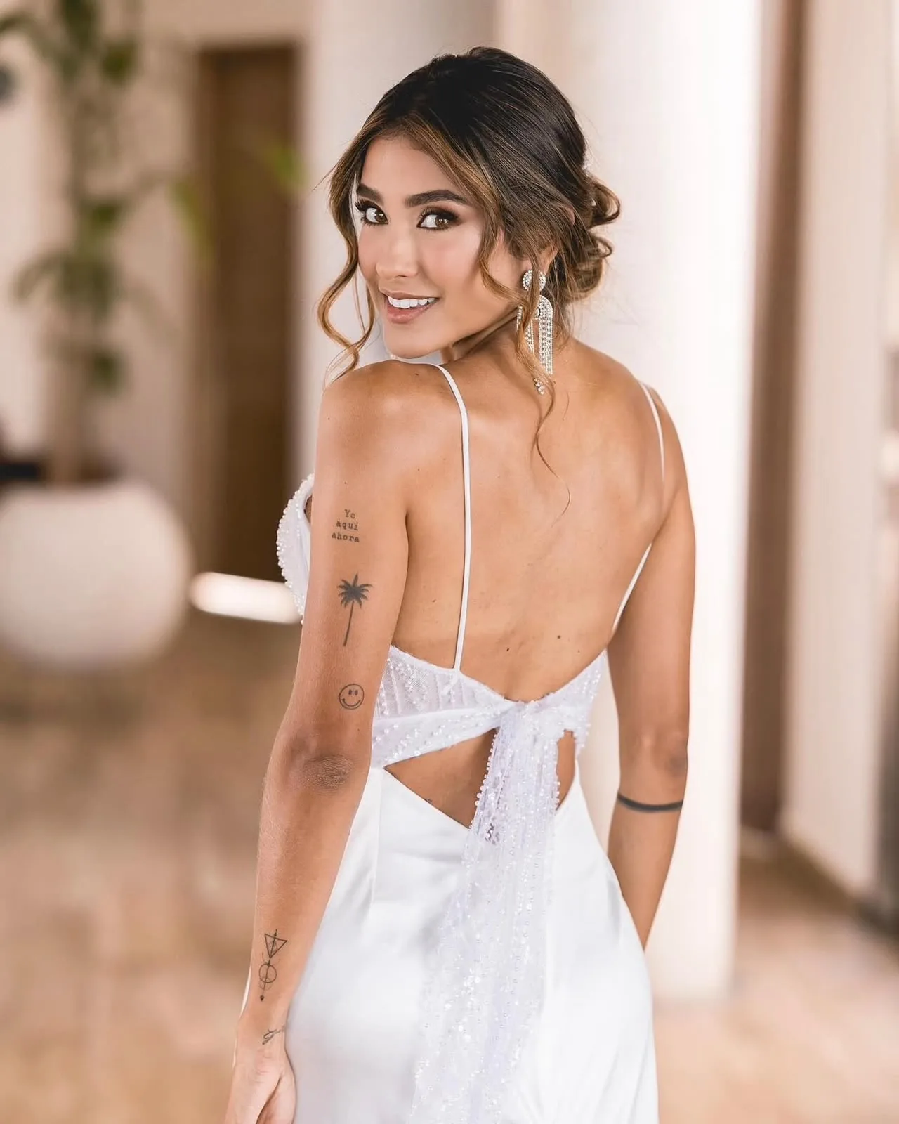Bride in an open-back gown looking over her shoulder in an indoor hallway