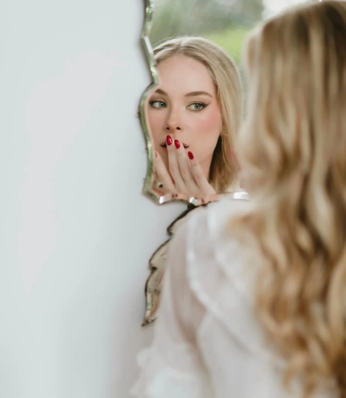Bride looking at her reflection in a vintage mirror, wearing red nail polish