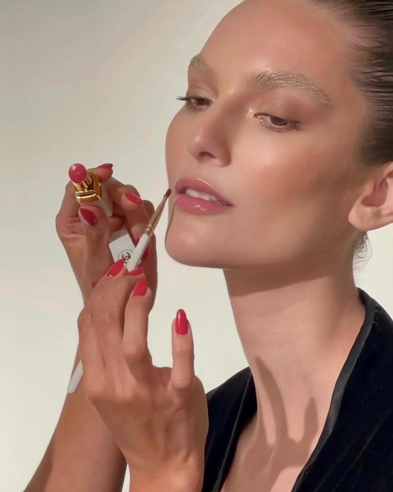 Close-up of red lipstick being applied with a brush, matching manicure