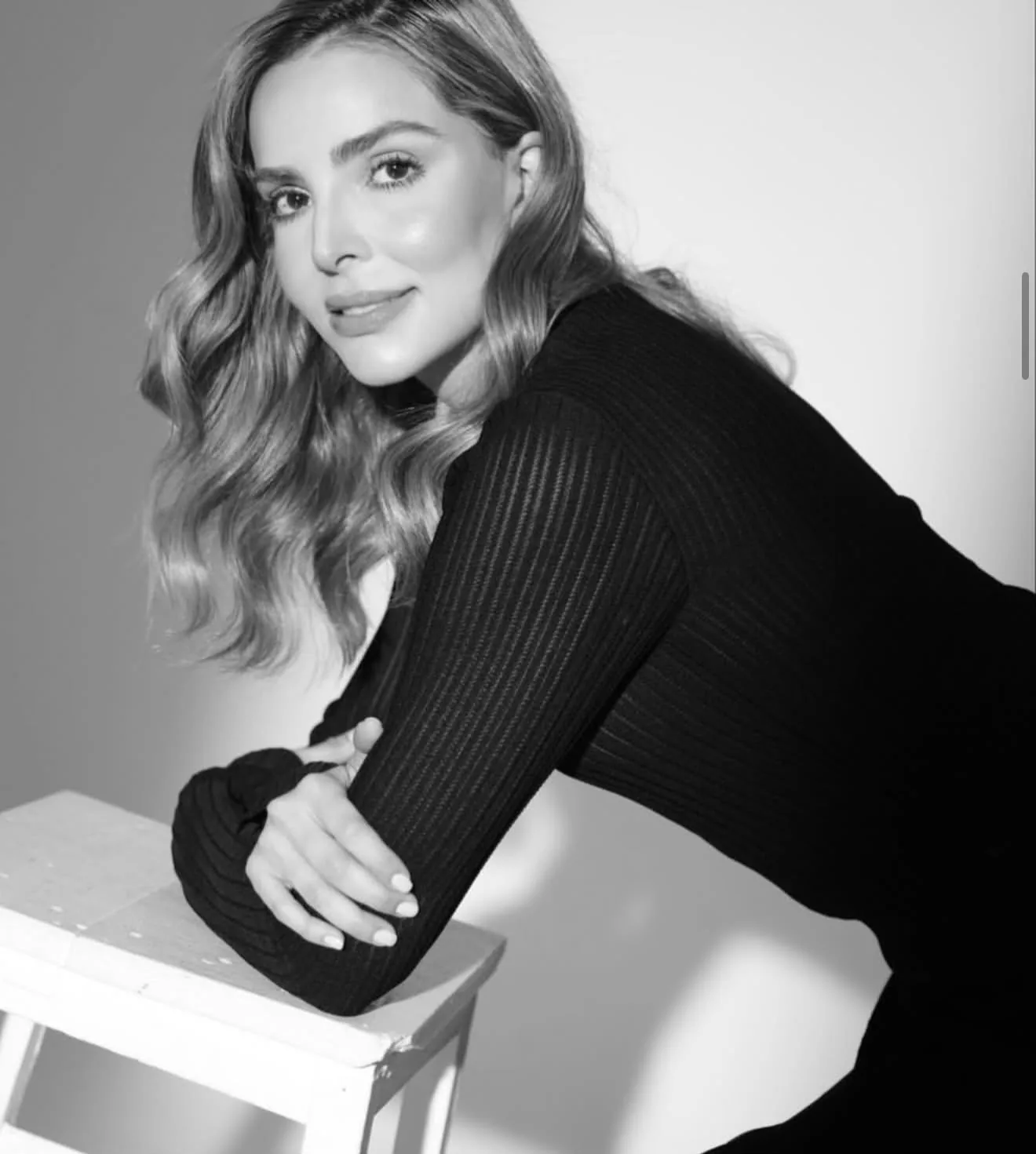 Black and white editorial portrait leaning on a stool, wavy hair